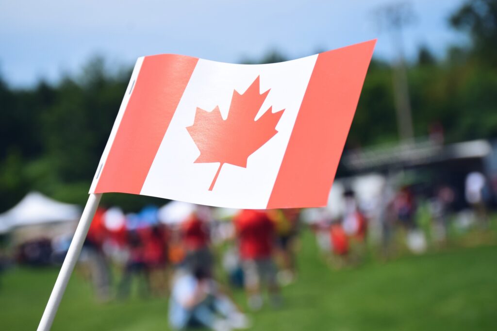 A Canadian flag with blurred fairgrounds in the background. Happy Canada Day